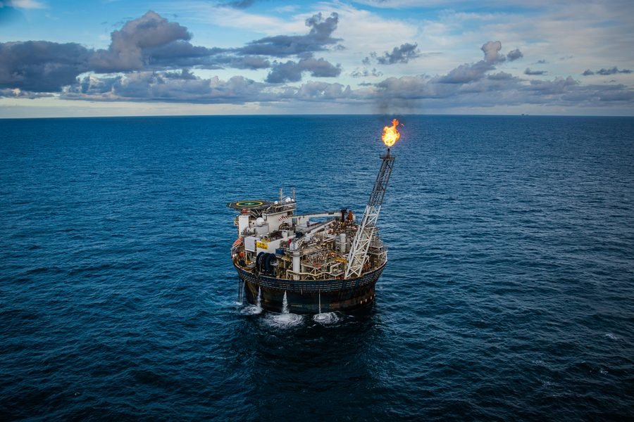 An offshore oil production platform at sea, gas flare burning from its boom.