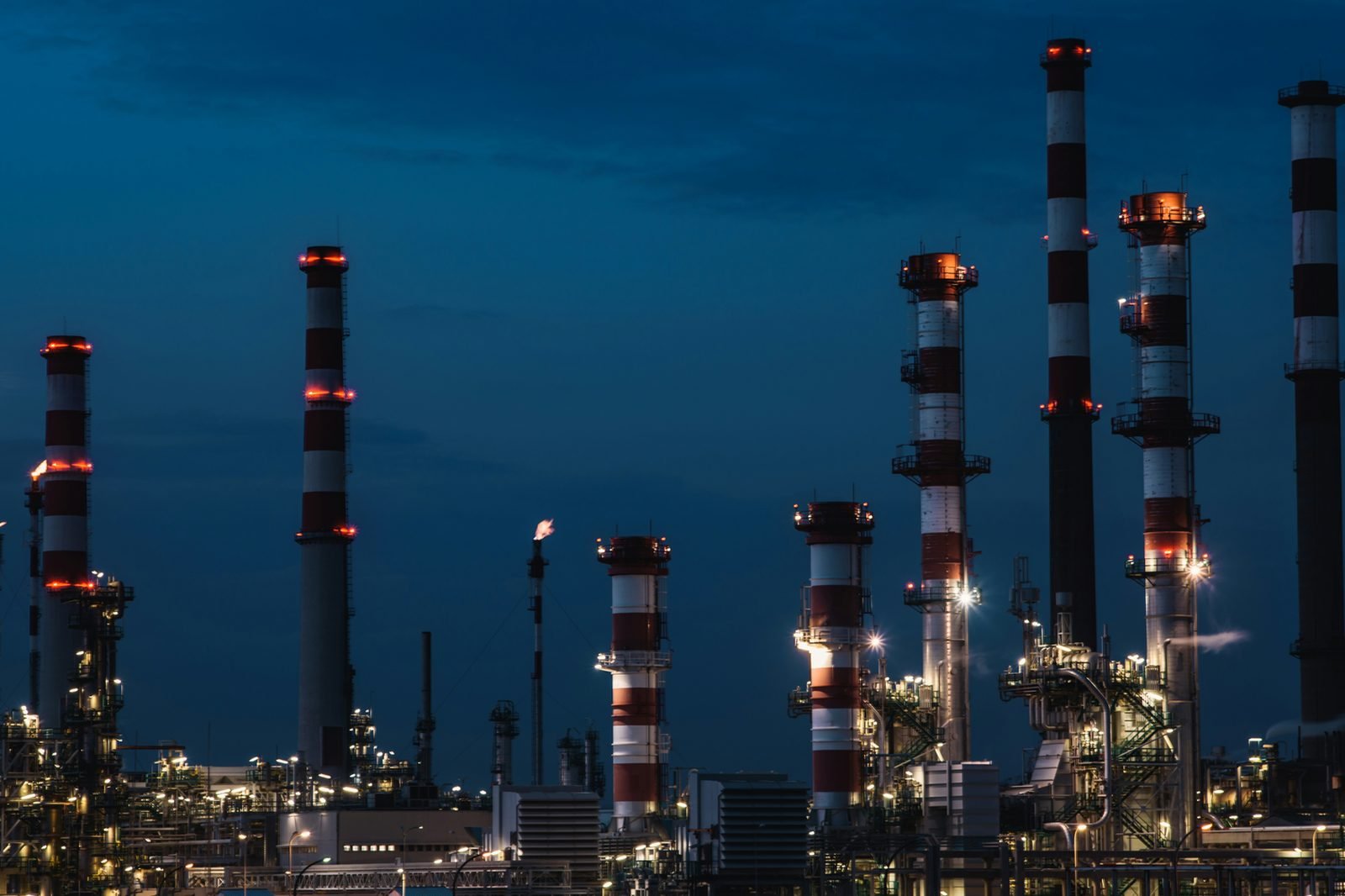 A power plant at dusk, lit stacks against a deep blue sky.